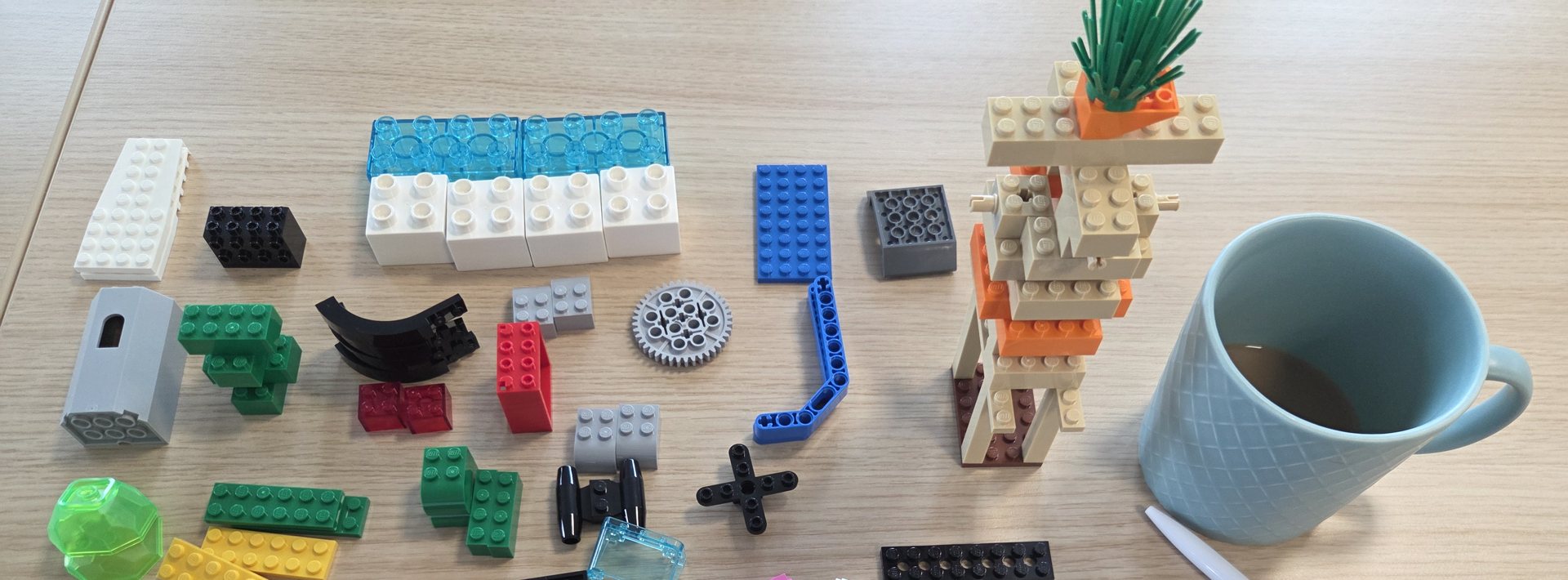 Sortierte LEGO-Steine auf einem Holztisch, daneben ein kleiner gebauter Turm und eine Kaffeetasse